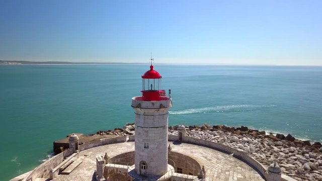 Aerial, orbit, drone shot, around Bugio lighthouse, on a rocky island, a boat in the background, on the atlantic ocean, on a sunny day, revealing the Oeiras coast, near Tejo river, in Lisbon, Portugal