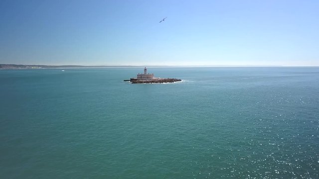 Aerial, reverse, drone shot, away from Bugio lighthouse, on a rocky island, on the atlantic ocean, on a sunny day, near the Oeiras coast and Tejo river, in Lisbon, Portugal