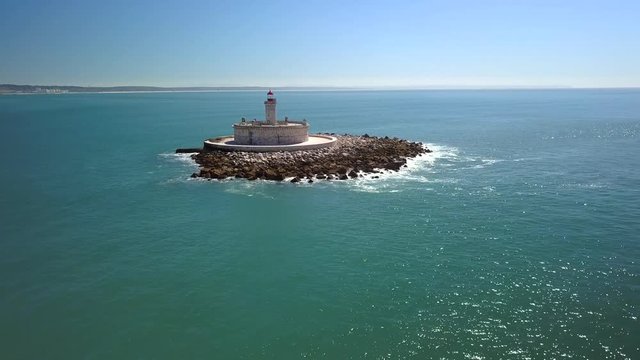 Aerial, reverse, drone shot, away from Bugio lighthouse, on a rocky island, on the atlantic ocean, on a sunny day, near the Oeiras coast and Tejo river, in Lisbon, Portugal
