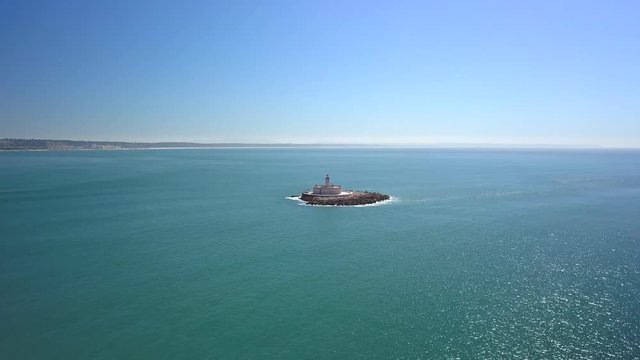Aerial, drone shot, towards Bugio lighthouse, on a rocky island, at the atlantic ocean, on a sunny day, near the Oeiras coast and Tejo river, in Lisbon, Portugal