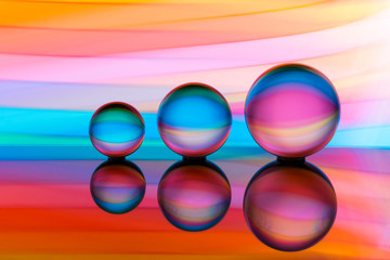 A row of three crystal balls with multicolored light painting behind them