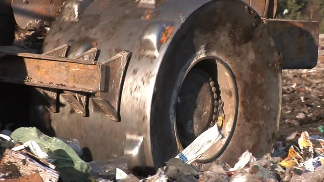Wheel of a bulldozer driving through the unsorted trash on a landfill site.