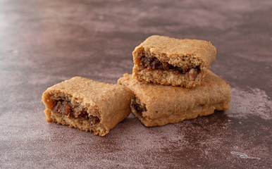 Side view of a blueberry fig bar broken in half on a whole bar atop a maroon background.