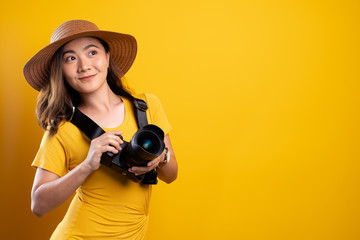 Woman in summer hat standing with photo camera isolated over yellow background