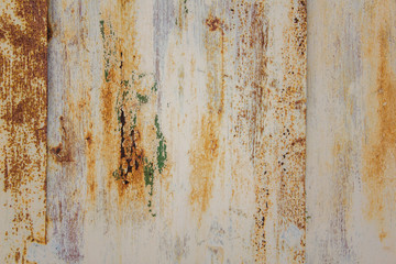 white peeling metal wall with scratches and stains of brown rust and green paint. rough surface texture