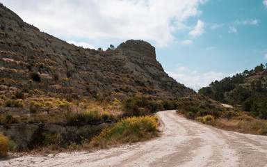 Dirt path by the mountain on a sunny cloudy day with bluee bright sky