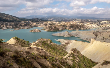 Lake on desser like mountain with eroded rocks with blue cloudy sky