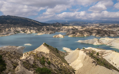 Lake on desser like mountain with eroded rocks with blue cloudy sky