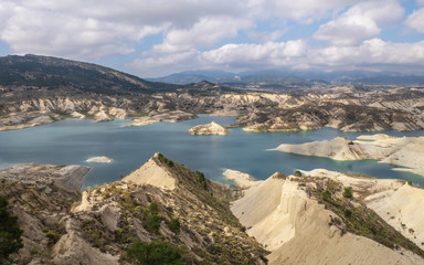 Lake on desser like mountain with eroded rocks with blue cloudy sky