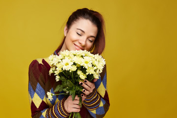 Happy birthday attractive female receives present from colleague, has overjoyed pleasant face expression, holds bouquet of flowers tenderly, feeling grateful and happy, closing eyes and smiles gently.