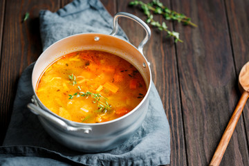 Spring vegetable soup with chicken stock in a pot on kitchen wooden table. Rustic style, close-up view.