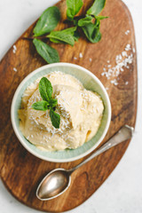 Top view of homemade vegan ice cream in a bowl is made from frozen mango and coconut milk served by fresh mint and flakes on a wooden textured board.