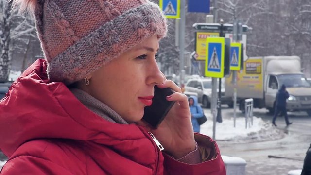 Portrait of a young woman talking on the phone while walking in the snowy winter city. Slow motion