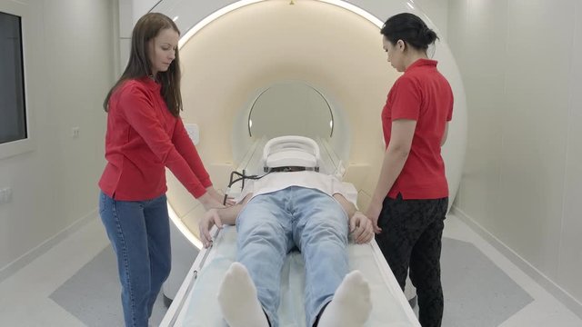 Magnetic resonance imaging machine scanning man head. Internship medicine program. Doctor showing to young female intern how does work modern clinic technology equipment MRI scanner with patient