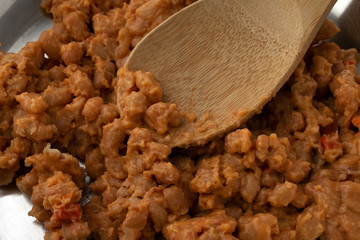 Baked beans with bacon in a tomato sauce with a wood spoon in the food.