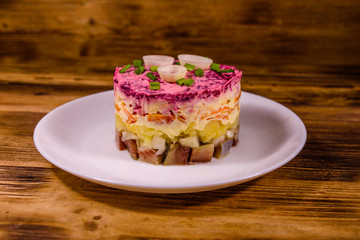 White plate with russian traditional new year salad herring under fur coat on wooden table