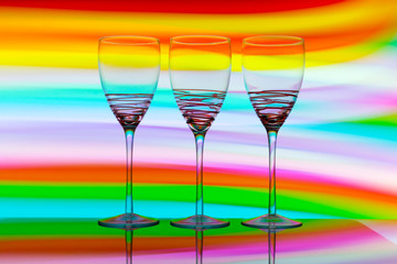 Three empty wine glasses in a row with colorful light painting behind