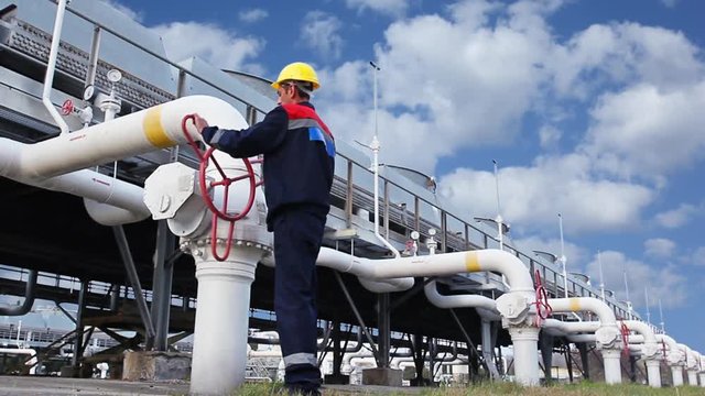 worker opens ball valve on cooling installations at gas compressor station, against background of cloudy sky