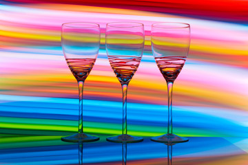 Three empty wine glasses in a row with colorful light painting behind