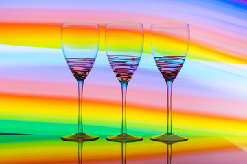 Three empty wine glasses in a row with colorful light painting behind