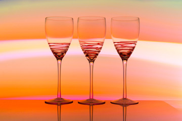 Three empty wine glasses in a row with colorful light painting behind