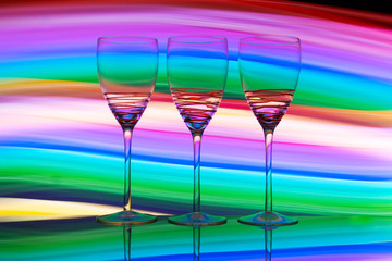 Three empty wine glasses in a row with colorful light painting behind