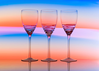 Three empty wine glasses in a row with colorful light painting behind