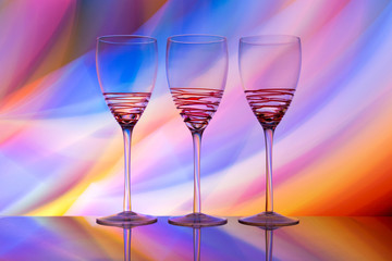 Three empty wine glasses in a row with colorful light painting behind