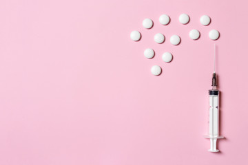 Syringe with white tablets as a injection and vaccination metaphor on pink background, flat lay, copy space