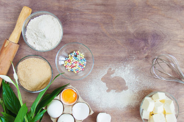 Products, kitchen appliances and tools on wooden table in the process of preparing Easter cookies dessert, cake. Trace of flour or powdered sugar in the form of rabbit. Top view flatlay, copy space