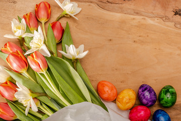 Bunte Blumen Tulpen und Narzissen sowie gefärbte Ostereier auf einem Holzbrett