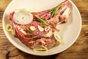 Marinated beef rib eye steak on bone with spices, onion and rosemary on wooden table