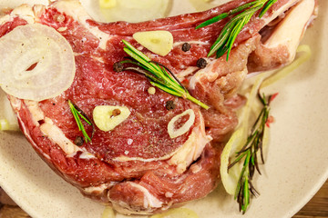 Marinated beef rib eye steak on bone with spices, onion and rosemary on wooden table