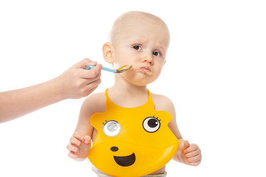 Baby boy does not want to eat porridge spoon mashed. Infant baby posing in yellow bib Isolated on white background. family, food, eating and people concept