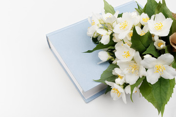 Closed book and jasmine flowers. A bouquet of flowers on a blue book on a white background.