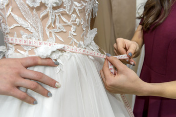 Female hands with measuring tape on waist of wedding dress
