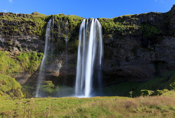 Wonderful view of Seljalandsfoss Waterfall in Iceland. Sunlight day in summer with rainbow and green landscape. Famous landmark on the route number one.