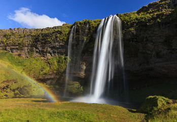 Wonderful view of Seljalandsfoss Waterfall in Iceland. Sunlight day in summer with rainbow and green landscape. Famous landmark on the route number one.