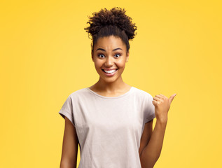 Overjoyed girl points aside, shows something at freespace. Photo of african american girl wears...