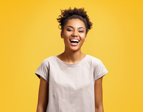 Joyful student laughs at good joke. Photo of african american girl wears casual outfit on yellow background. Emotions and pleasant feelings concept.