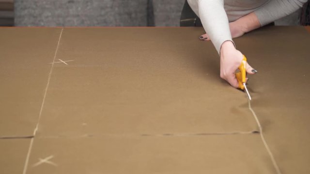 A tailor cutting a high quality brown fabric using professional scissors and squaring cut pieces of fabric
