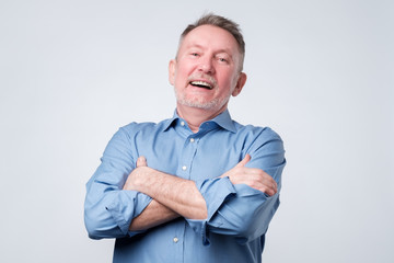 Old man in blue shirt folding arms, looking away and smiling