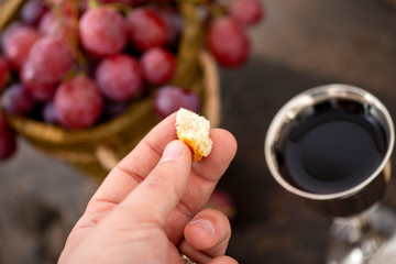 Man breaking the bread, with wine, grapes and Bible in the background