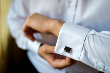 Obraz na płótnie Canvas Hands of wedding groom buttoning up his white shirt. Male's hands on a background of a white shirt, sleeve shirt with cufflinks. Close-up