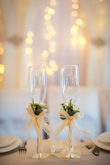 Two empty wedding champagne glasses with creamy bows and flower decor on the table. Glasses for groom and bride.