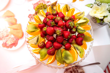Delicious fruits in plate on a festive table. Healthy fresh fruit platter with strawberries, oranges and kiwis on a wedding table. Close-up
