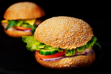 Two big burgers with beef and vegetables on the dark background. Fresh tasty sandwiches with green lettuce. Unhealthy food. Close-up