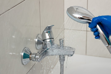 Close-up of the shower faucet and shower head cleaning process from lime scale, white chalk sediment and stains using a commercial soap scum remover. Bathroom cleaning and disinfection, cleanup