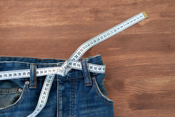 Jeans with a measuring tape on a green background. Weight loss concept