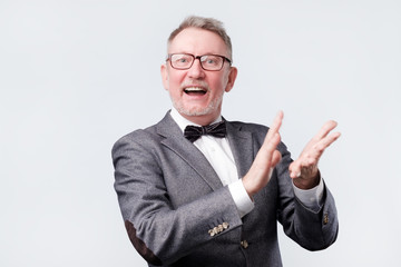 Handsome senior man in glasses and suit applauding